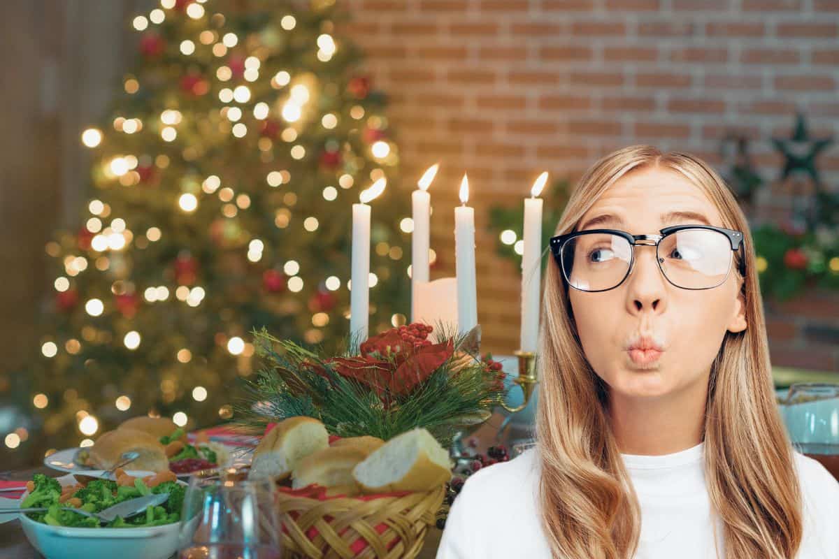 tavola apparecchiata con sfondo albero di natale e una donna con espressione colpevole